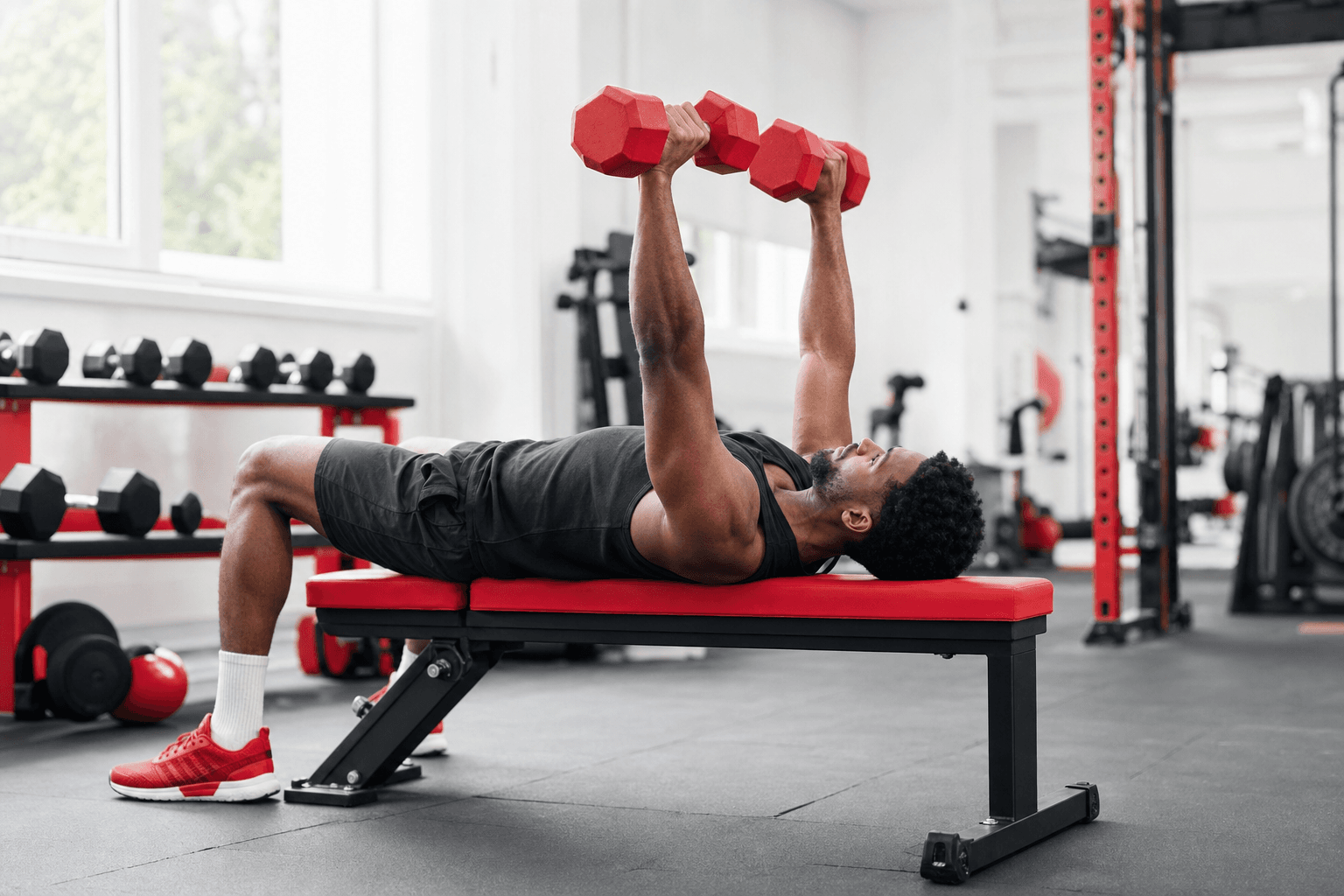 Lean athlete seated on an adjustable bench with dumbbells, plates, resistance band, and rack in a dark garage gym